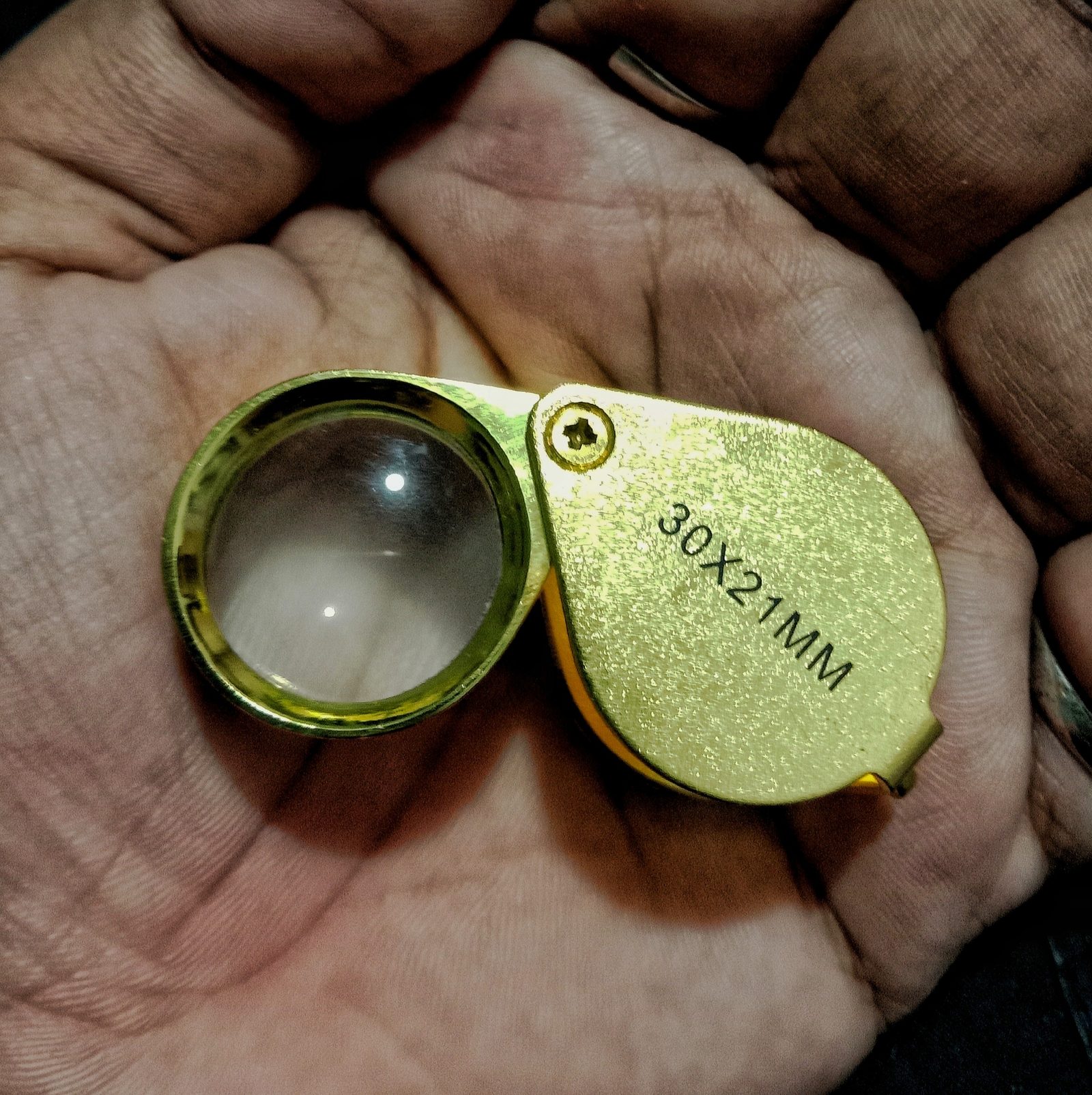 A jeweler's 10x triplet loupe held open in a hand, the tool used to read a girdle inscription