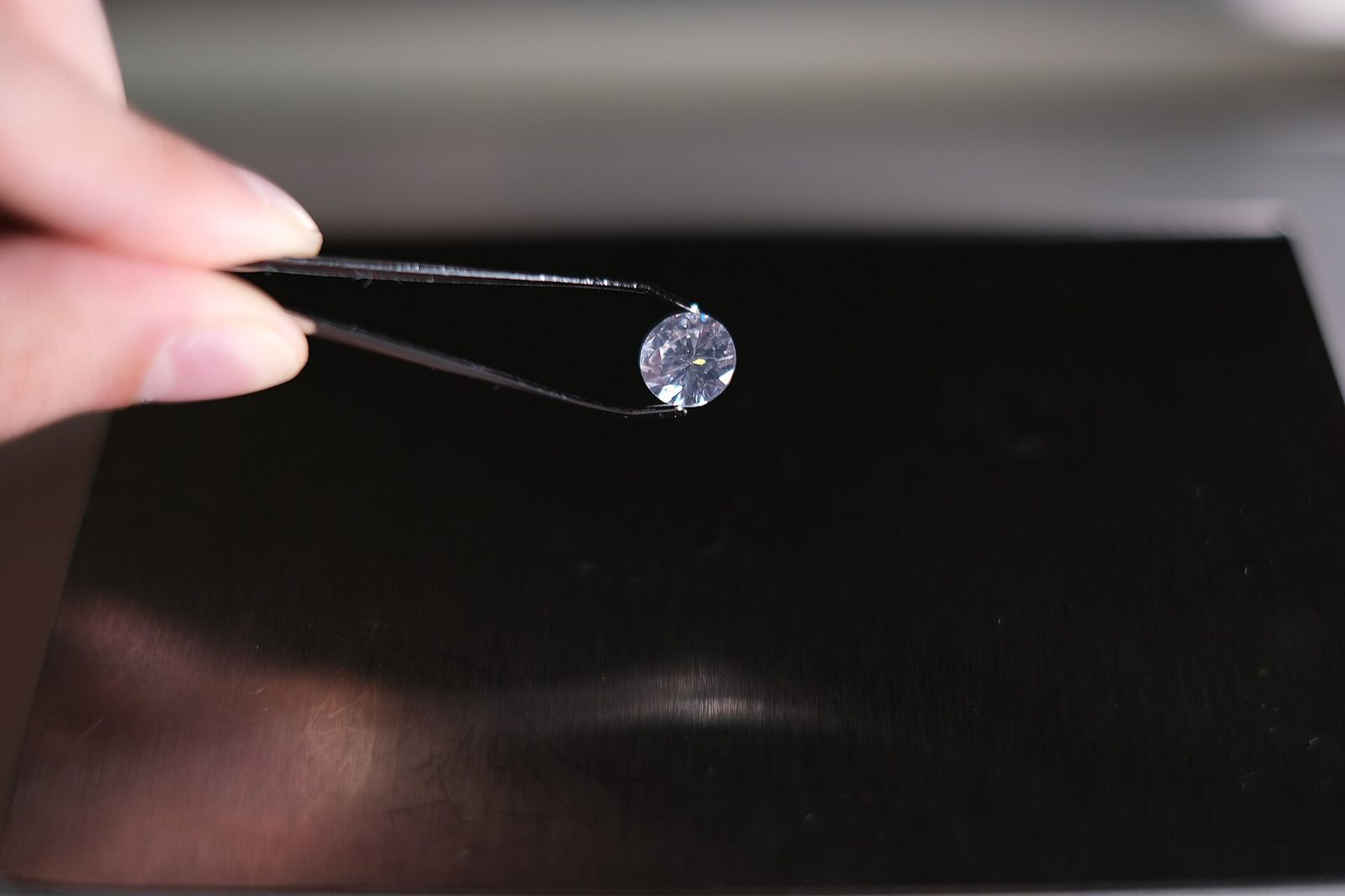 A loose round brilliant diamond held in tweezers for close visual examination against a dark background.