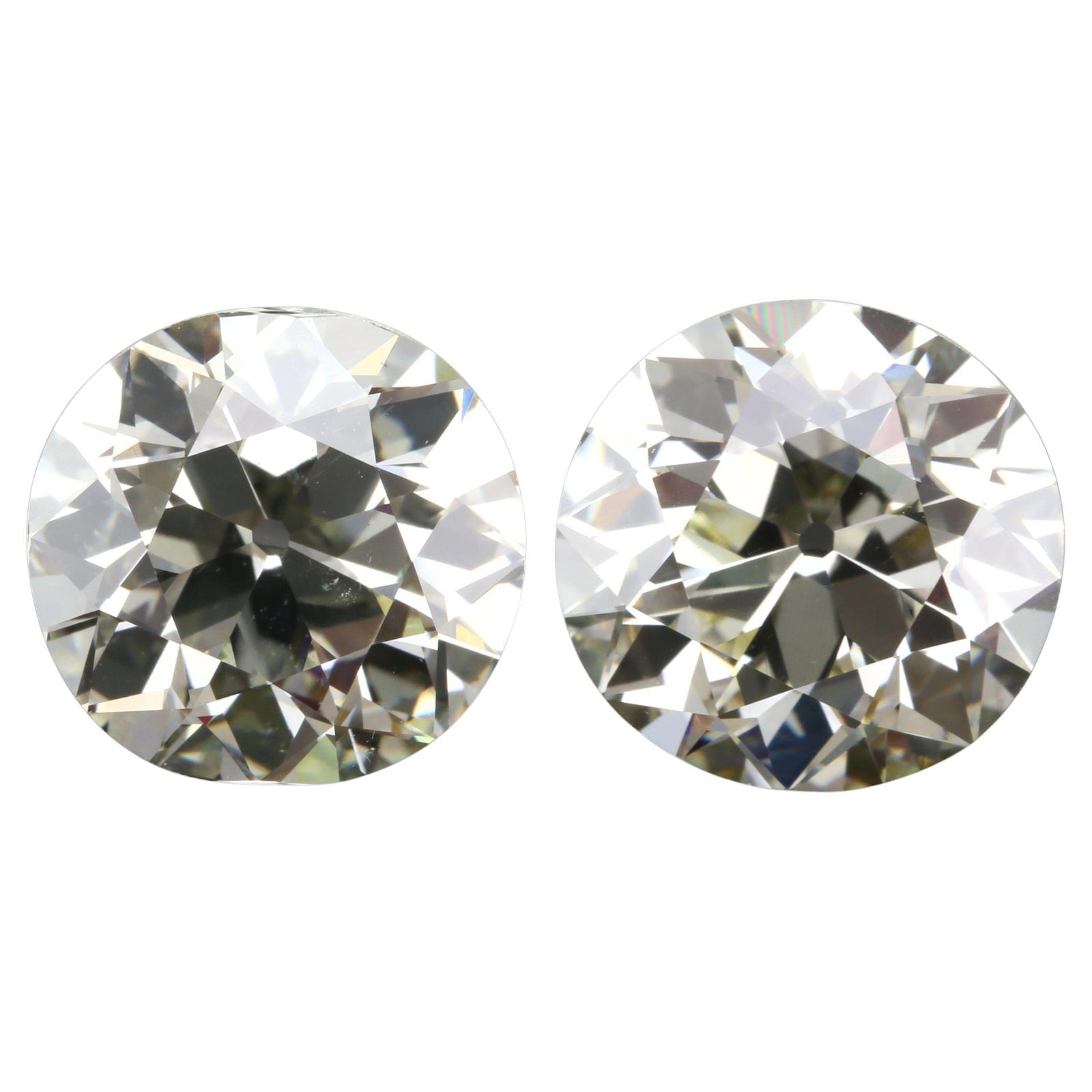 Two large old European cut diamonds photographed face up and side by side on a white background with a narrow gap between them, both round in outline, both showing an open culet as a dark dot at the center, chunky triangular facets and the same warm grey and olive tones.