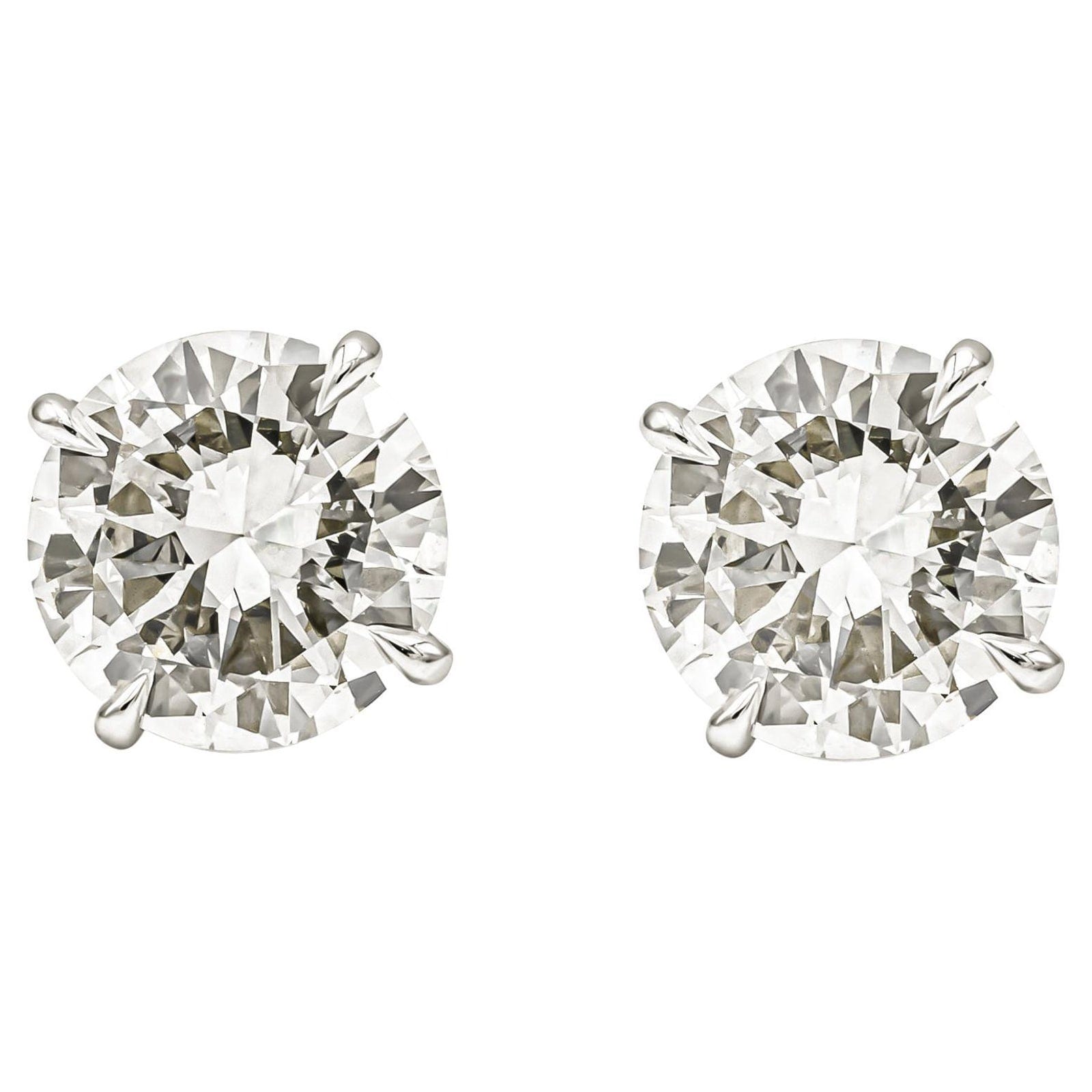 Two round brilliant diamonds set in white metal four prong stud mounts, sitting side by side and face up on a white background at almost the same diameter and the same flash pattern.