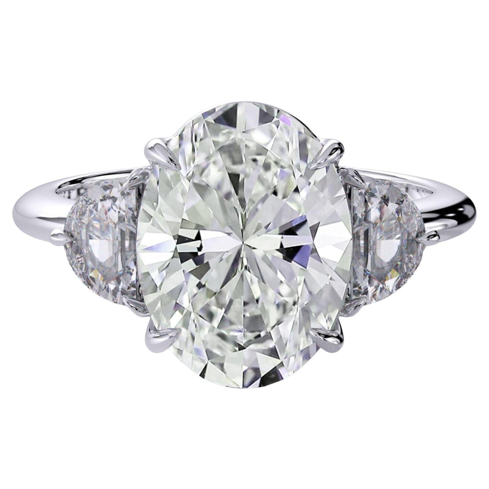 A white metal three stone ring photographed from directly above, a large oval brilliant in the middle with a half moon diamond on each side, each half moon turning its straight edge toward the oval and its curved edge toward the shank.