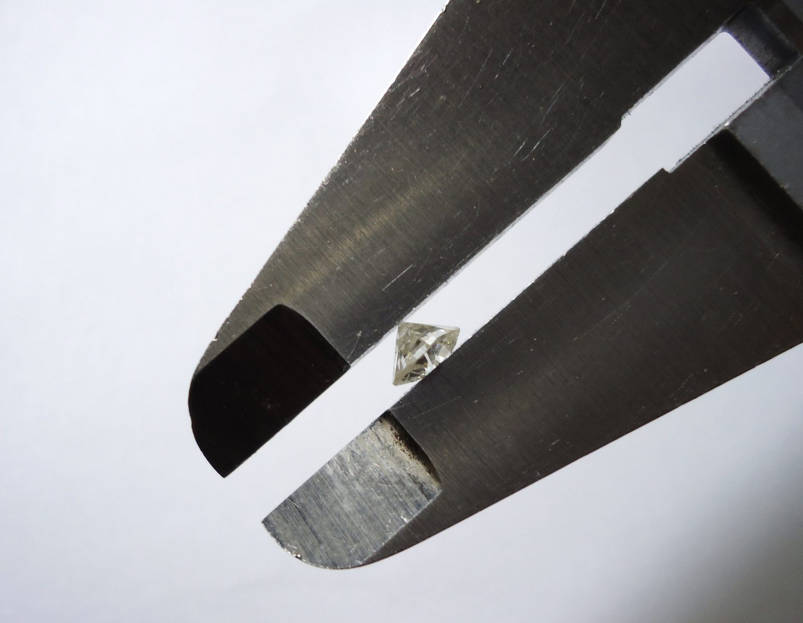 A loose diamond held between the jaws of a digital caliper to read its millimeter measurements