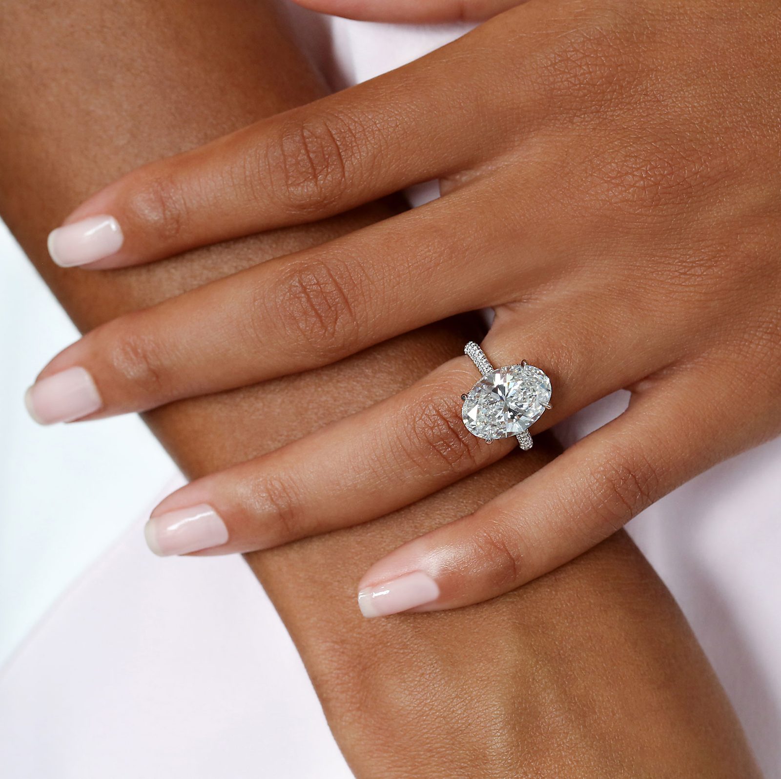 An oval cut diamond solitaire ring on a hand, showing the elongated rounded outline that a length to width ratio describes