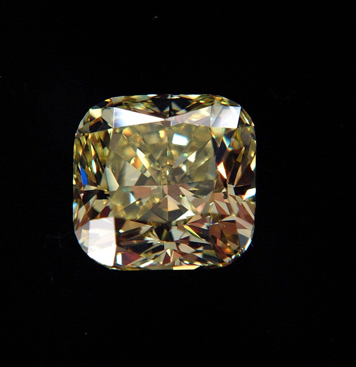 A loose cushion cut diamond with soft rounded corners and pillow shaped facets, photographed on a black background
