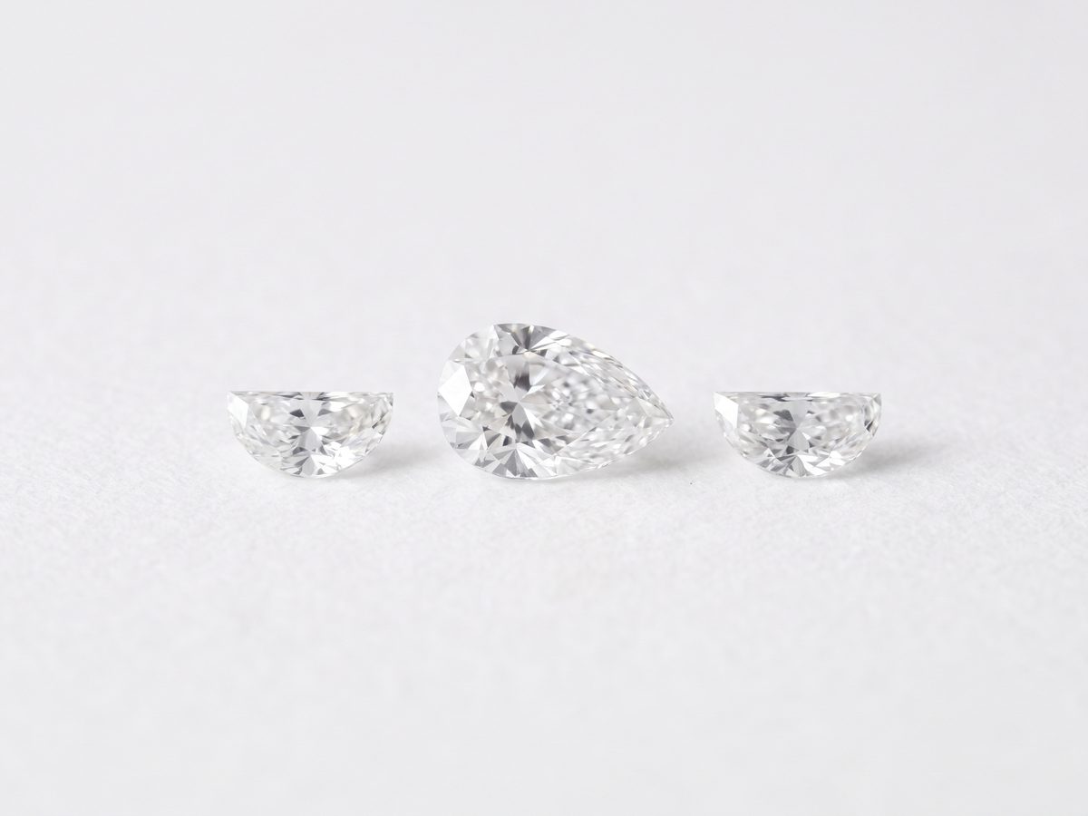 A pear shaped center with two half moon side stones laid on white paper under a daylight lamp