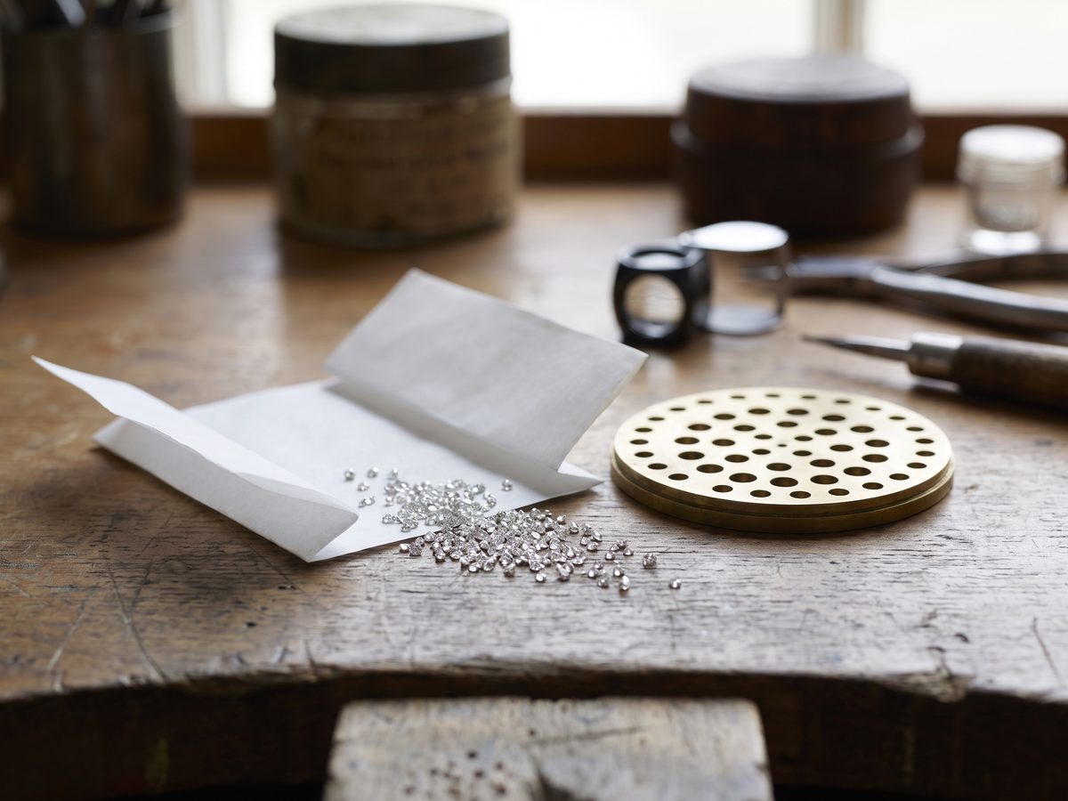 A small pile of melee diamonds in an open white stone paper next to a metal sieve plate