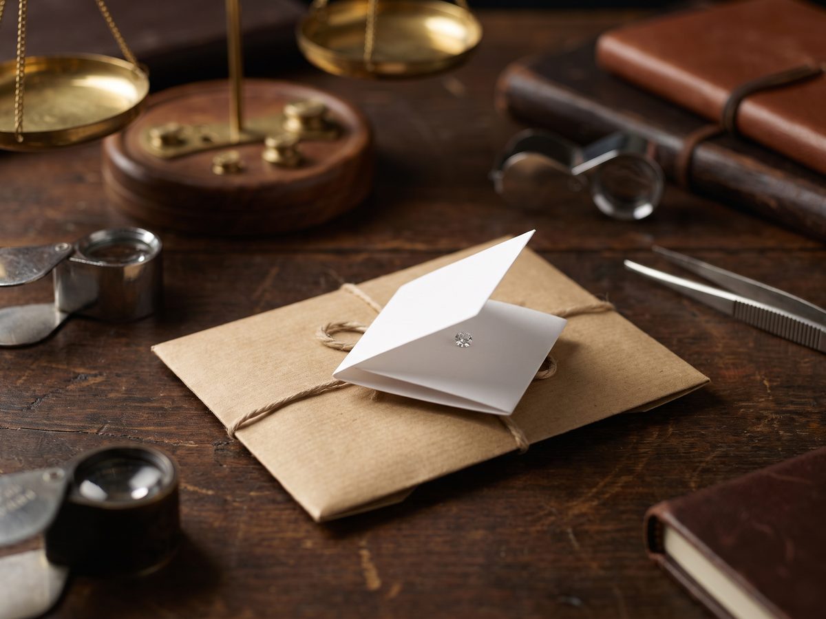 A memo parcel envelope opened to show folded stone papers beside a small brass carat scale