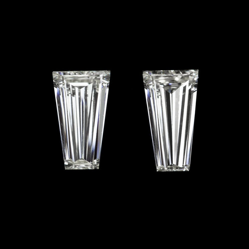 Two loose tapered baguette diamonds standing side by side against a black background, each a long four sided step cut that narrows from a wide end to a narrow end, their parallel facet rows running at the same angle on both stones