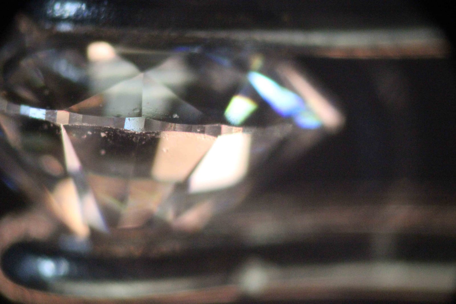 Microscope view across the waist of a polished diamond, with crown facets sloping in from above, pavilion facets falling away below, and a narrow band of small polished faces running horizontally between them.