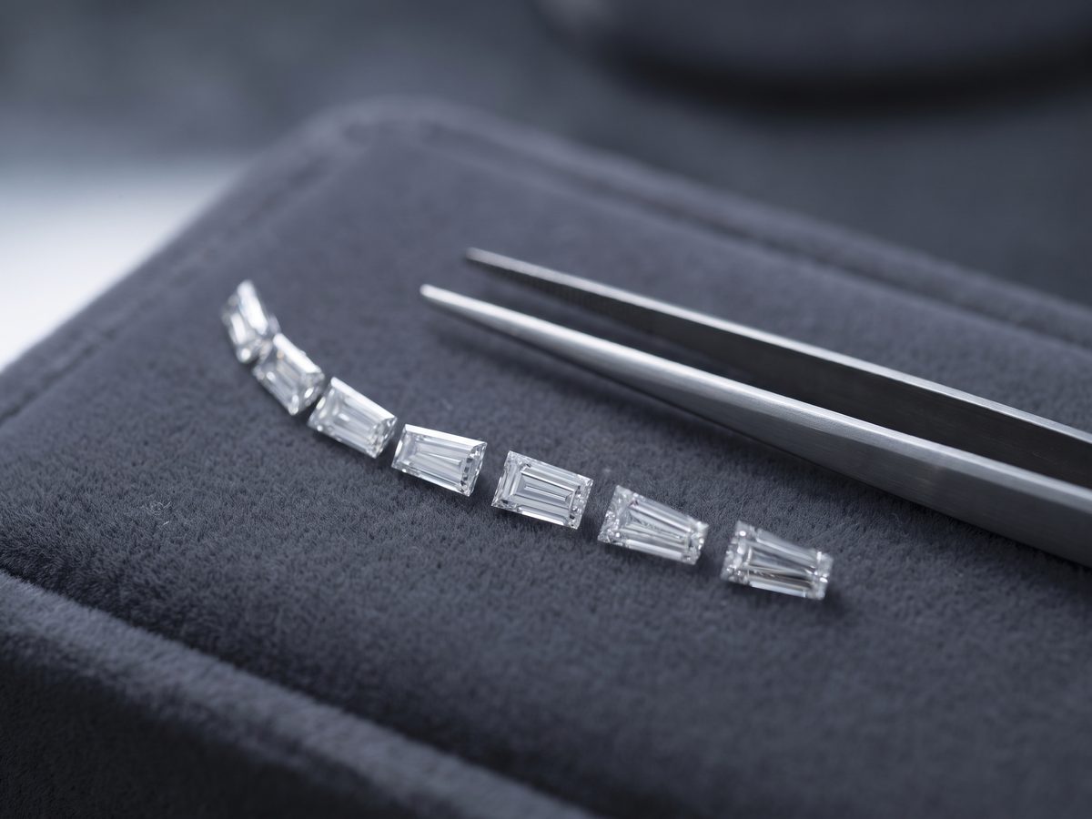 A row of loose tapered baguettes fanned across black velvet with a pair of tweezers resting beside them