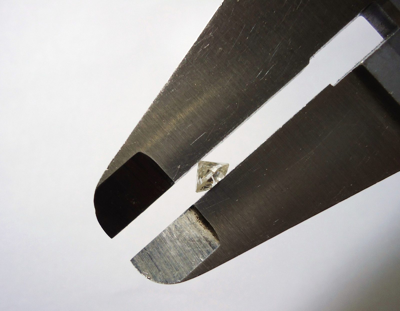 A loose diamond held between the jaws of a caliper for a millimeter measurement, photographed against a white background